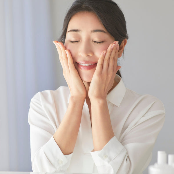 Woman in a white shirt with hands on face against a light background