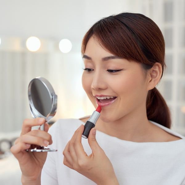 Woman applying lipstick in front of a mirror