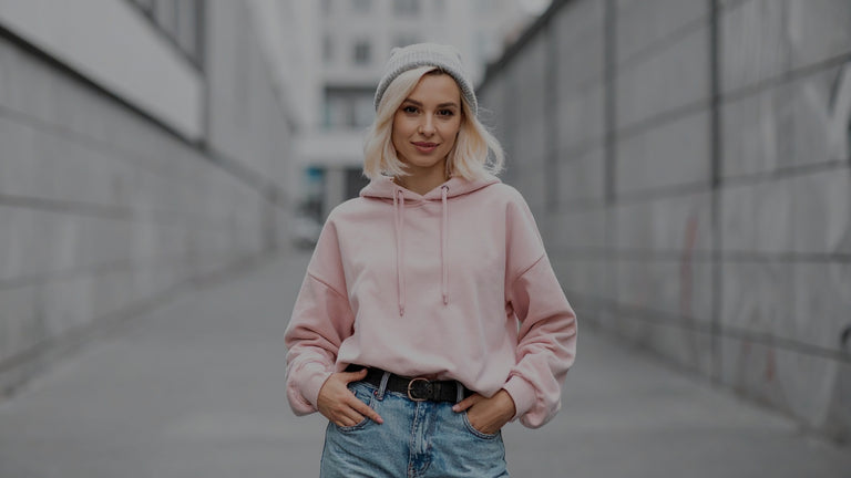 Person wearing a pink hoodie and blue jeans standing in an urban setting